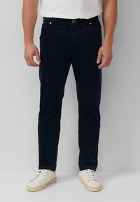 Marineblauwe chinos van zacht materiaal met een slim fit, voorzien van voorzakken en gestikte details, gecombineerd met witte sneakers.