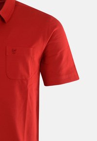 Rød polo-shirt lavet af bomuld med en struktureret finish, der har en enkelt brystlomme og et subtilt logo broderet på lommen.