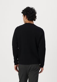 Schwarzer Pullover mit langen Ärmeln aus weichem Strickmaterial, mit klassischem Rundhalsausschnitt und lässiger Passform, getragen mit grauen Hosen.