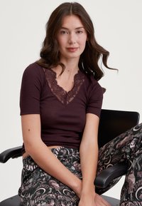 Bordeaux ribbed korte mouwen top met een kant V-hals detail, gedragen met zwarte gestippelde broek met bloemen- en hemelse ontwerpen.