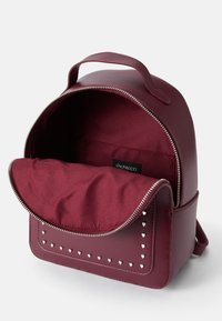 Sac à dos en simili cuir bordeaux avec fermeture éclair, doublure en tissu, compartiment avant et détails en clous en forme de cœur sur le rabat.