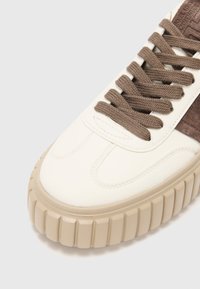 Basket en cuir blanc avec des accents en suede marron, lacets texturés et une épaisse semelle beige avec des détails en design cannelé.