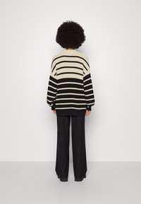 Pull oversize à rayures noires et crème avec manches ballon, col et ourlet côtelés. Associé à un pantalon noir ample.