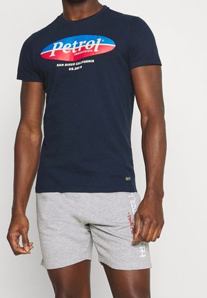 T-shirt en coton bleu marine avec un logo graphique audacieux en rouge et bleu. Assorti à un short gris, présentant une texture légère et une coupe décontractée.