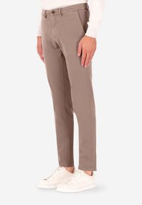 Pantaloni chino in cotone beige dal taglio slim, con chiusura a bottoni e tasche laterali, abbinati a sneakers bianche. Tessuto liscio e linee pulite.