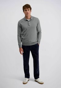 Grijze polo met lange mouwen en een kraag, voorzien van drie knopen, gecombineerd met marineblauwe corduroybroek. Witte sneakers met beige accenten.