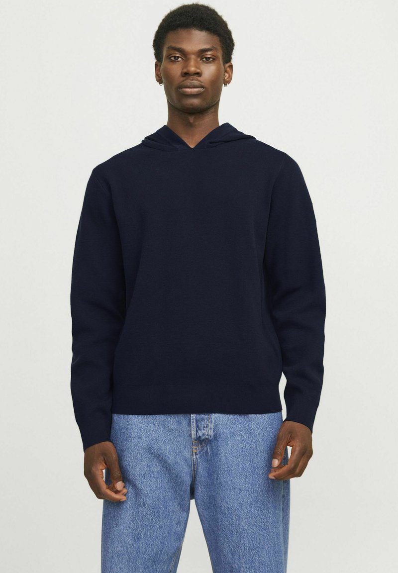 Felpa blu navy con design a V, realizzata in tessuto morbido, con maniche lunghe e orlo a coste, indossata con jeans azzurri.