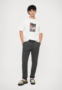 Camiseta blanca de algodón con estampado gráfico, combinada con joggers de punto grises y zapatos bicolor con cordones y suela gruesa.