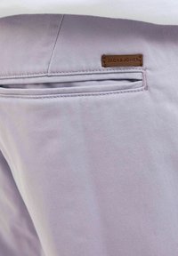 Lichtpaarse broek met een gladde textuur, voorzien van een achterzak en een bruine leren label met de tekst "JACK & JONES."