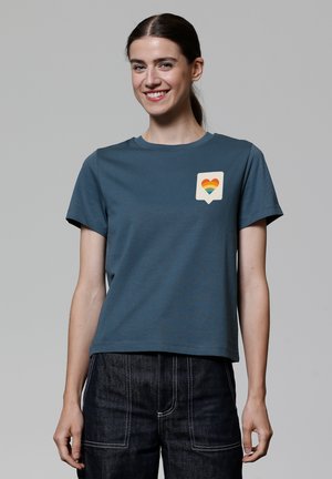 T-shirt en coton bleu avec col rond et manches courtes, arborant un motif de bulle de dialogue crème avec un cœur arc-en-ciel.