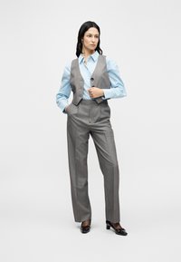 Κοστούμι γκρι με ρίγες, με εφαρμοστή γιλέκο και παντελόνια με φαρδιά πόδια, σε συνδυασμό με ανοιχτό μπλε πουκάμισο με κουμπιά και σκούρα παπούτσια με τακούνι.