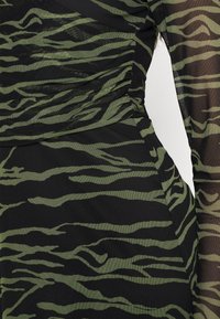 Mustan kankaan kanssa vihreät tiikeri raidat, jotka ovat teksturoitu pinta ja kootut yksityiskohdat sivuilla, luoden istuvan siluetin.