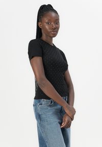 Black short-sleeve top with a ribbed texture and scattered silver accents. Fitted design, crew neck, paired with blue jeans.
