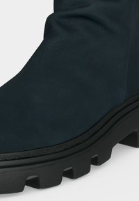 Gros plan d'une botte noire avec un matériau supérieur texturé et une semelle épaisse en caoutchouc à crampons pour une meilleure adhérence et durabilité.