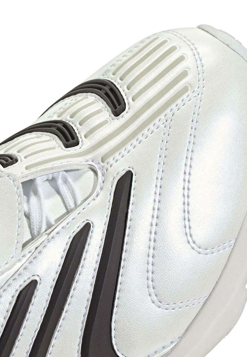 Nahaufnahme eines weißen Sneakers mit schwarzen und grauen Akzenten, der detaillierte Nähte, eine strukturierte Sohle und weiße Schnürsenkel zeigt.