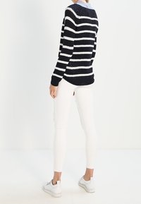 Suéter a rayas azul marino y blanco con mangas largas, textura de punto; combinado con pantalones blancos y zapatillas blancas, visto desde atrás.