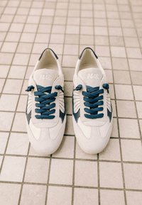 Paire de baskets P448 blanches et bleues avec des lacets bleu foncé posée sur un sol carrelé clair vue de dessus.