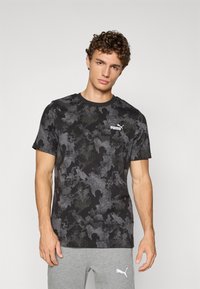 Zwart en grijs camouflage t-shirt met korte mouwen, ronde halslijn en Puma-logo op de bovenste linkerzijde. Zachte stoftextuur.