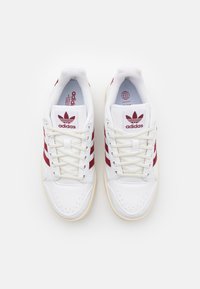 Vita sneakers med röd tre-stripes design, perforerat tåparti och krämfärgad gummisula. Har broderad logga och snörning.