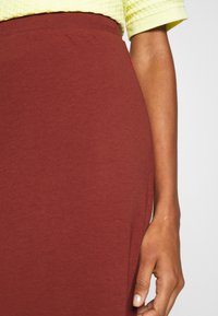 Bordeaux nederdel med en glat tekstur og elastisk talje, parret med en lys gul, struktureret kortærmet top.