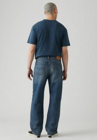 T-shirt a girocollo blu abbinata a jeans in denim blu a vestibilità morbida, con un'etichetta in pelle marrone sul retro e gambe dritte.