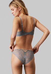 Ensemble en grey en dentelle comprenant un soutien-gorge et un string, avec des motifs ondulés et des détails délicats. Bretelles réglables et fermeture à crochet dans le dos.