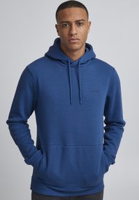 Sudadera de algodón azul con un bolsillo frontal, capucha con cordón, puños acanalados y un pequeño logo en el pecho. Textura suave y corte clásico.