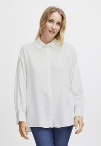 Camicia bianca con colletto, maniche lunghe e taglio morbido. Realizzata in tessuto leggero con una texture liscia.