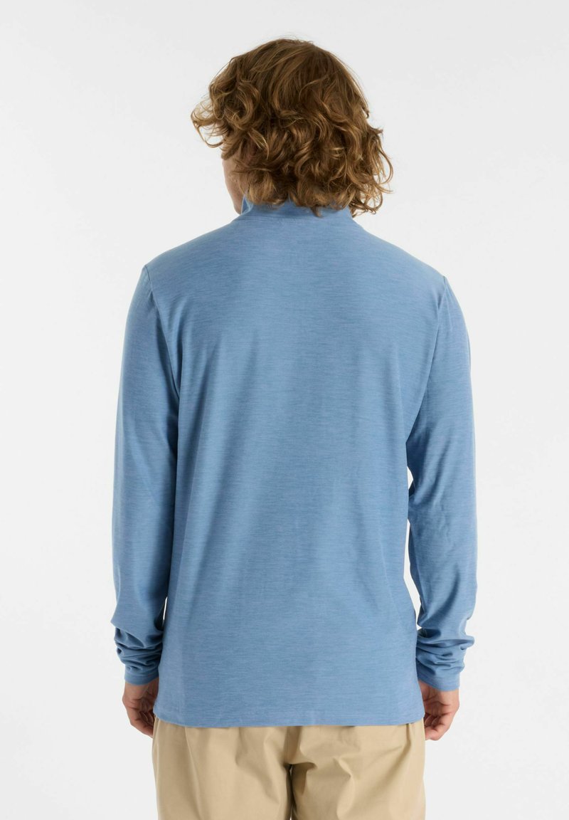 Chemise à manches longues bleu clair avec un col haut et une coupe décontractée. Texture douce, design minimal et ourlet légèrement incurvé.