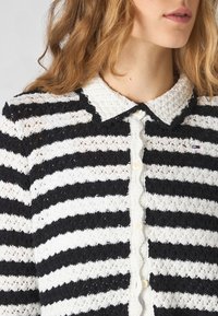Svart- och vitt randig kardi med en vågig krage och knappstängning, med en texturerad stickad design.