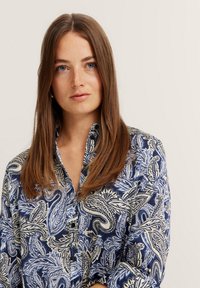 Navy blue shirt with a contrasting white paisley pattern, button-down collar, and long sleeves. Smooth fabric with a glossy finish.