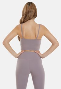 Light lavender sports bra with thin straps, fitted design, and smooth texture, paired with matching high-waisted leggings.