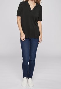 Černá pletená polo košile s výstřihem do V a krátkým rukávem, kombinovaná s tmavě modrými slim-fit džíny a bílými teniskami.