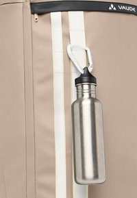 Beige stof tas met witte accentstrepen en een gestructureerd oppervlak, met een zilveren metalen waterfles eraan bevestigd met een zwarte dop en een karabijnhaak.
