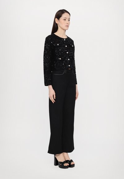 Jachetă neagră cu paiete, cu detalii de nasturi, combinată cu pantaloni negri largi și sandale cu platformă. Textură fină și siluetă elegantă.
