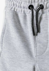 Pantaloni jogger in cotone grigio con vita regolabile tramite un cordoncino intrecciato bianco e nero, tasche laterali e tessuto morbido e testurizzato.