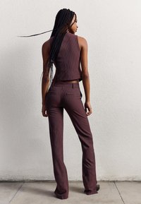 Burgundy two-piece outfit with vertical stripes; cropped sleeveless top and fitted pants; smooth texture; subtle pockets; minimalistic design.