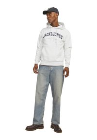 Sudadera gris con el logo "JACK & JONES", vaqueros azules holgados y botas de cuero oscuras. La sudadera tiene cordón y bajo de canalé.