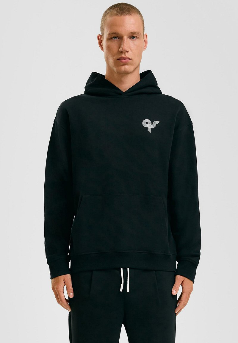 Zwarte capuchontrui gemaakt van zachte stof, met een voorzak en een klein grafisch logo op de linkerborst. Textured afwerking.