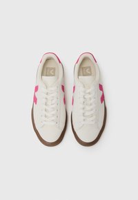 Hvite sneakers med rosa semsket akenter, med en rund tå, snøring og brunt gummisåle. Logoet er synlig på tungen.
