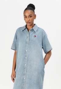 Denimskjortklänning i ljusblått med korta ärmar, knäppning framtill och logotypapplikation. Avslappnad passform och mjuk textur.
