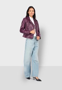 Kožená motorkářská bunda v tmavě fialové barvě, s zipy a švy, v kombinaci s světle modrými širokými džíny a černými lodičkami s špičatou špičkou.