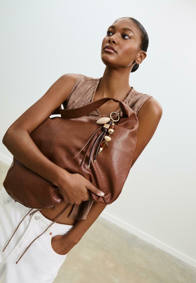 Sac à main en cuir marron à la conception décontractée, orné de perles décoratives et d'un porte-clés. Dispose de poignées doubles et d'une surface texturée.