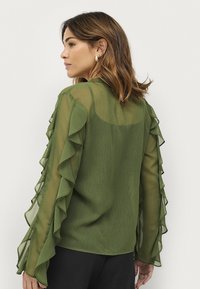 Grøn chiffon bluse med rynkede lange ærmer, subtil struktur, en afslappet pasform og et glat bagdesign. Pyntet med knapdetaljer.
