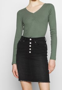 Grön randig långärmad topp med V-ringning och rynkdetalj, i kombination med en svart denimkjol med knappframsidan och fransad fåll.