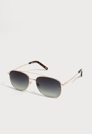 Lunettes de soleil aviateur à monture dorée avec verres foncés dégradés et branches aux extrémités à motif écaille sur fond clair.