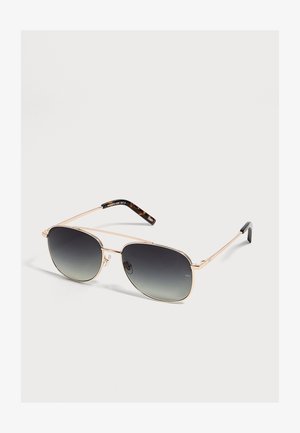 Lunettes de soleil aviateur à monture dorée avec verres foncés dégradés et branches aux extrémités à motif écaille sur fond clair.