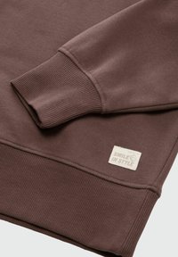 Brauner Baumwoll-Sweatshirt mit gerippten Bündchen und strukturiertem Finish. Ein Etikett mit "SMILE IN STYLE" ist am Saum angenäht.