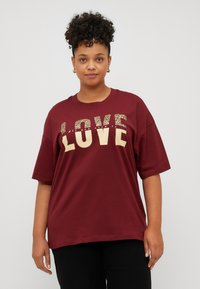 Maroon oversized t-shirt with leopard print and gold text saying "LOVE" on the front. Short sleeves and a round neckline, made of cotton.