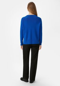 Royal blue sweter dzianinowy z ribbowymi mankietami i dołem, w połączeniu z czarnymi spodniami w prostym kroju. Tekstura wydaje się gładka, a wzór jest prosty i nowoczesny.